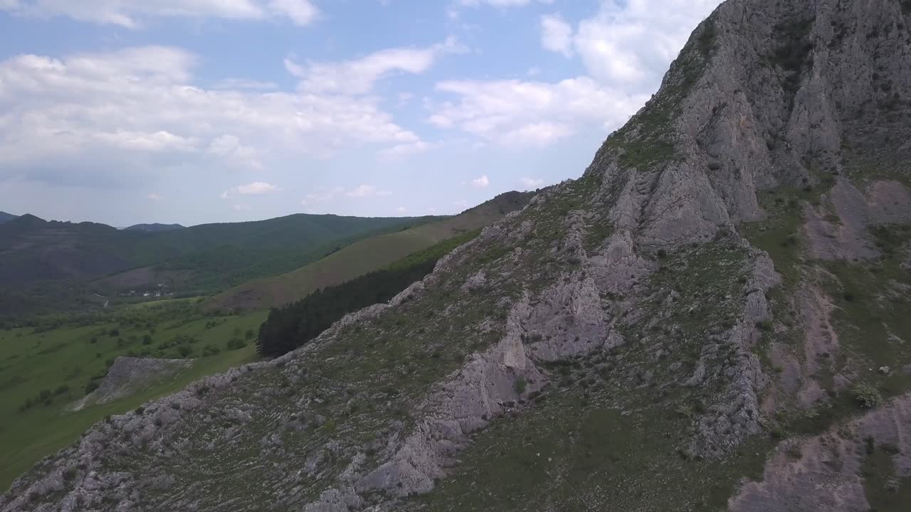 Drone Footage Of Hiker In The Distance Climbing Rocky Mountain With Green Valley In Horizon