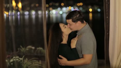 a romantic couple embracing and kissing by a window overlooking a night cityscape