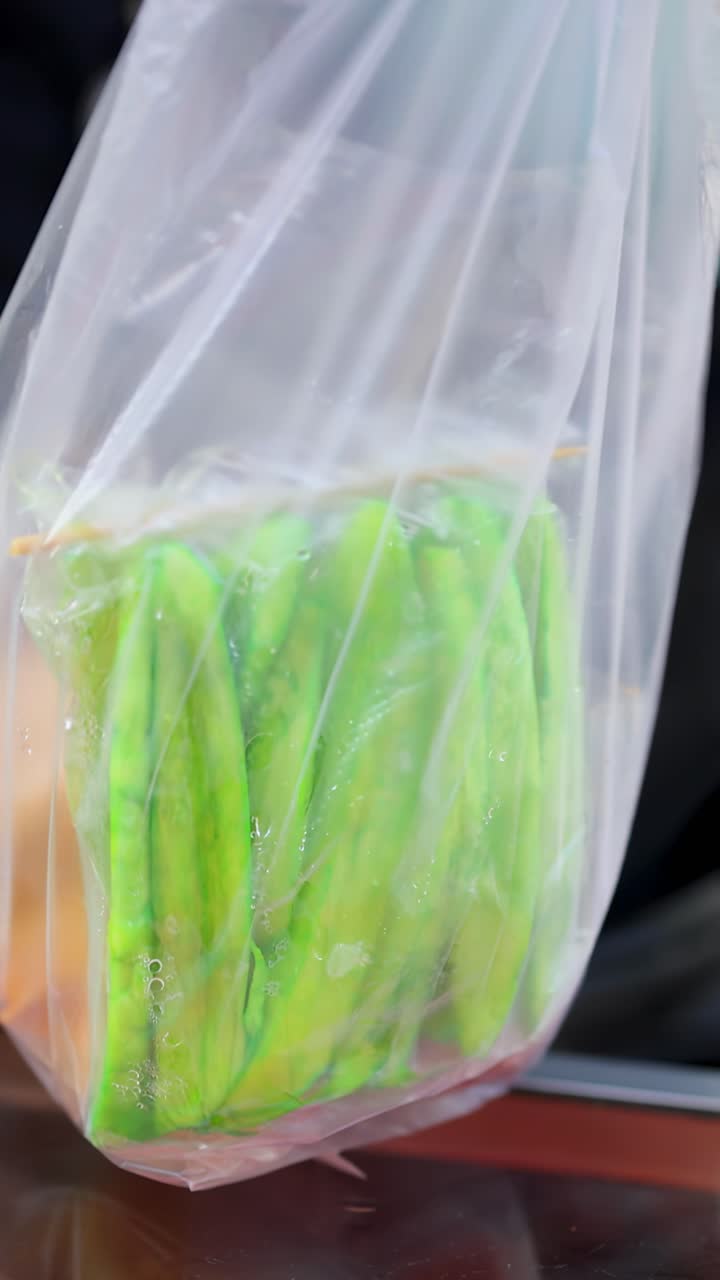 Mão enluvada de vendedor embala manga e mamão fatiados em saco plástico em mercado de rua ao ar livre em Bangkok.