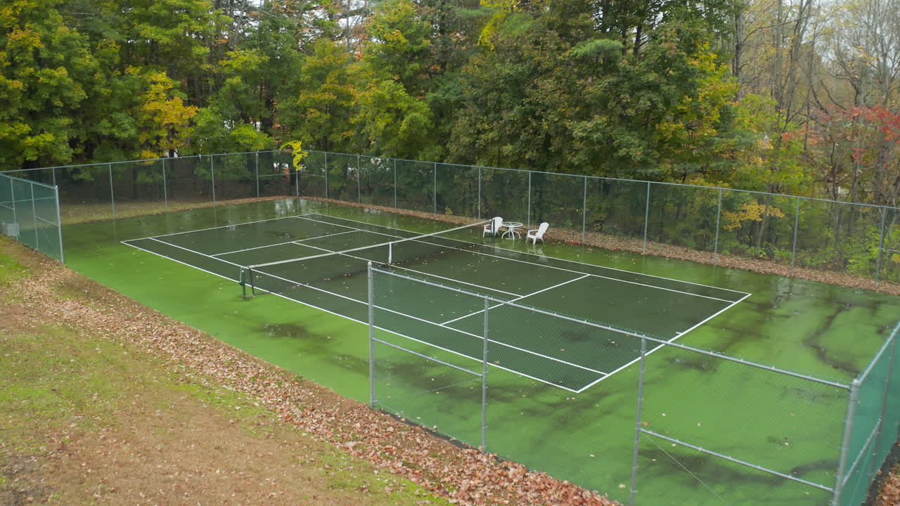 drone volando hacia una cancha de tenis húmeda y vacía en el follaje otoñal
