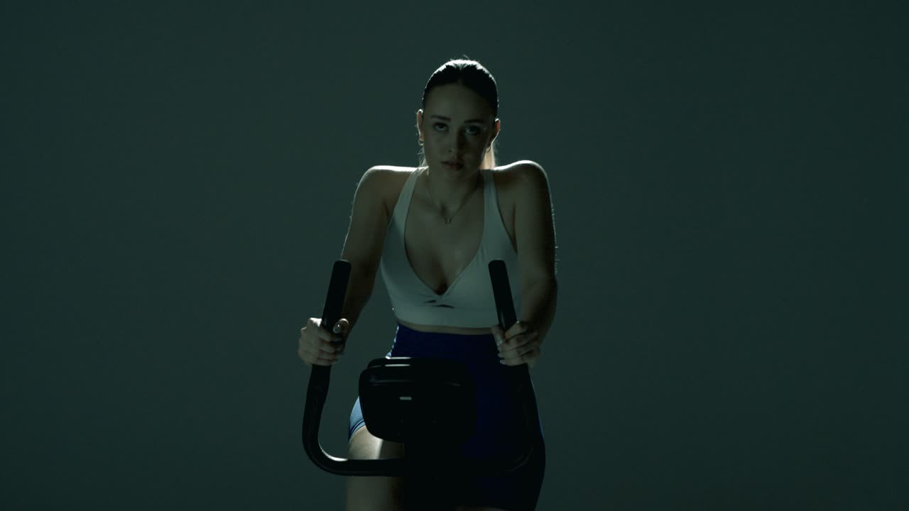 Smooth vertical tracking shot rising from the bottom of the bike and the woman’s pedaling feet, up past the handlebars to her shoulders and focused face, all lit by dramatic cinematic backlight