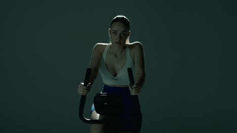 smooth vertical tracking shot rising from the bottom of the bike and the woman’s pedaling feet, up past the handlebars to her shoulders and focused face, all lit by dramatic cinematic backlight
