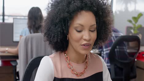 African-american-woman-talking-on-phone-headset-sitting-on-her-desk-at-office