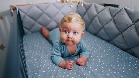 caucasian infant with adorable plump cheeks lies peacefully in the crib. lovely cute blue-eyed baby boy chewing something.