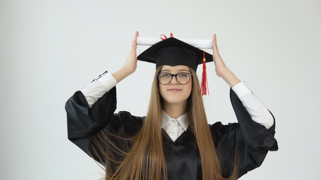 una mujer joven en la universidad en la capa del maestro recorta su diploma con las manos sobre la gota y se maravilla de la cámara. retrato en un fondo blanco