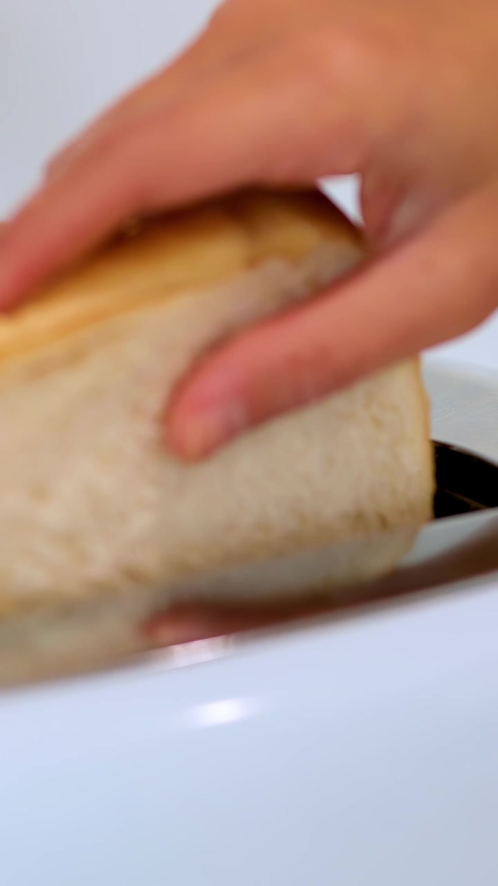 A person’s hands insert white bread slices into a shiny toaster in a brightly lit kitchen, captured in close-up with smooth camera movement