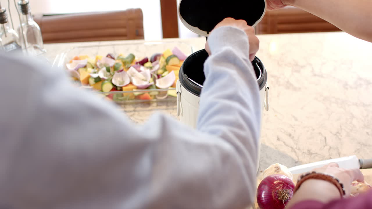 Composting food scraps in kitchen, multiracial gay couple practicing eco-friendly habits at home