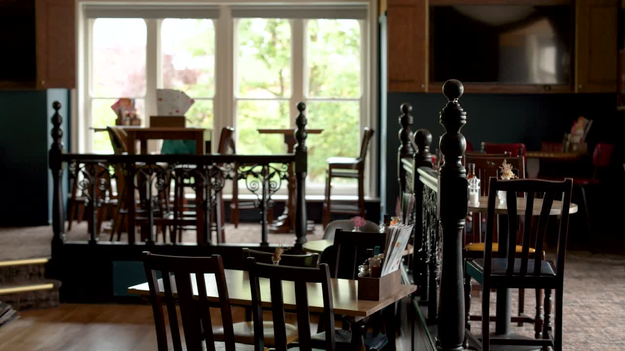 Camera slowly pans through warmly lit, empty wooden cafe with large windows and vintage decor