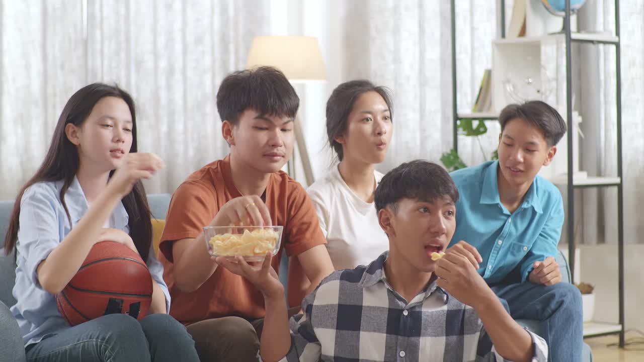 아시아 십대 들 이 집 에서 농구 경기 를 보고, 먹고, 응원 하고 있다