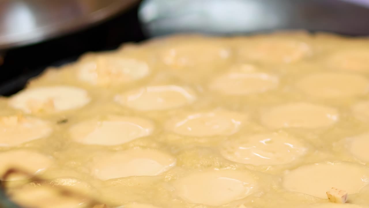 Close-up of batter being poured into circular molds on a hot surface.