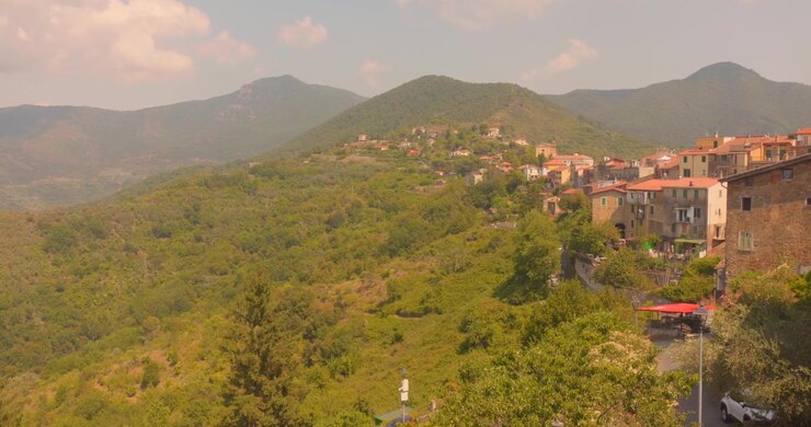 Il borgo collinare di Perinaldo si erge sopra verdi montagne ondulate in una calda e leggermente umida giornata estiva, Italia