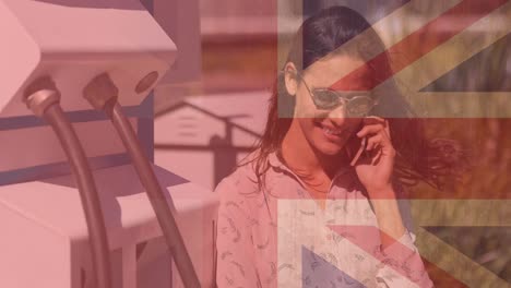 flag of great britain over smiling caucasian woman using smartphone and charging electric car