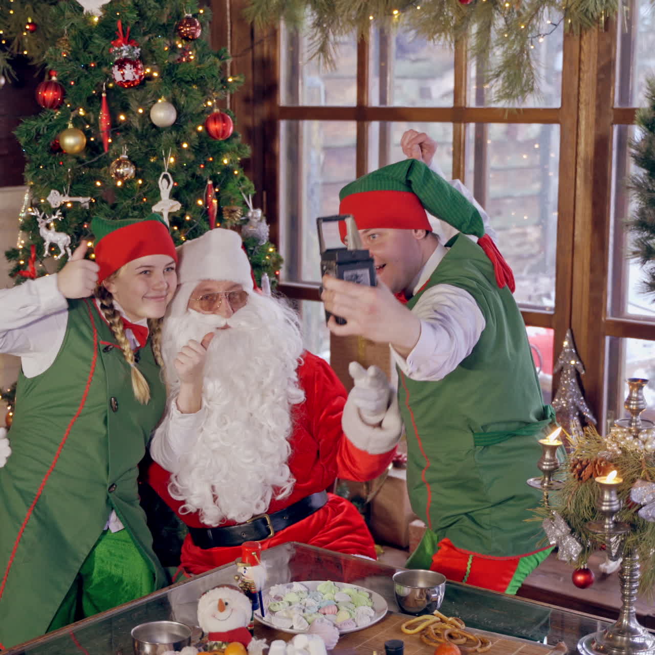 Happy elves and Santa near Christmas tree. Santa Claus together with joyful elves making photo. Fairy characters doing selfie at Christmas.
