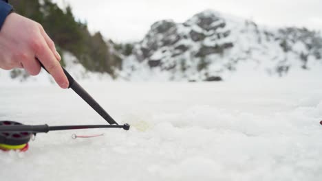 scooping snow from ice hole with fishing rod on ground in winter