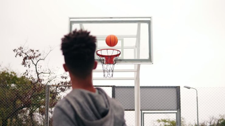 Young african player jumping up and throwing ball in a basketball hoop, the ball hits the ring and scores. The man turns around