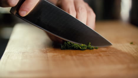 male hand placing chives on a cutting board, then starts to cut