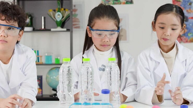 Kolme aasialaista opiskelijaa laboratoriotakeissa suorittamassa fysiikan koetta pingispalloilla.