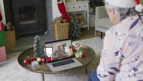 Ältere-Kaukasische-Frau-Winkt-Und-Benutzt-Laptop-Für-Weihnachtsvideoanruf-Mit-Mann-Auf-Dem-Bildschirm