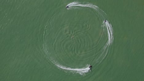 Three-jet-skis-riding-in-a-circle-on-lake,-aerial-top-down-view,-slomo