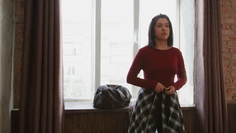 young woman tying a plaid shirt around her waist in a room