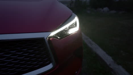 epic closeup shot of a red car with chrome detail and black grille with modern led headlight on during a cold slightly foggy night, crane down with tilt up