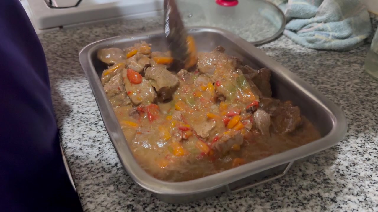 Un cuisinier transfère de la viande braisée dans une sauce riche avec des légumes mélangés dans un plat de service sur un comptoir de cuisine, révélant un repas fait maison fraîchement préparé, plan de révélation, gros plan avec faible profondeur de champ.