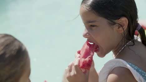 closeup of girls face while eating watermelon by swimming pool.