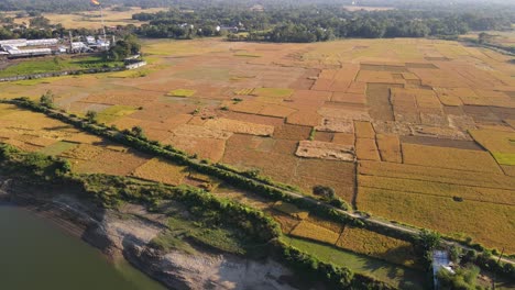 Tierras-De-Cultivo-Junto-A-Un-Río-Rodeado-De-Bosques-Con-Una-Planta-De-Gas-En-El-Fondo-Y-Un-Camino-Rural-A-Lo-Largo-Del-Río-En-Bangladesh