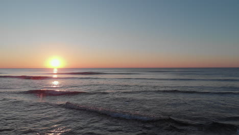 drone flying in ocean while rising morning sun is glowing in front