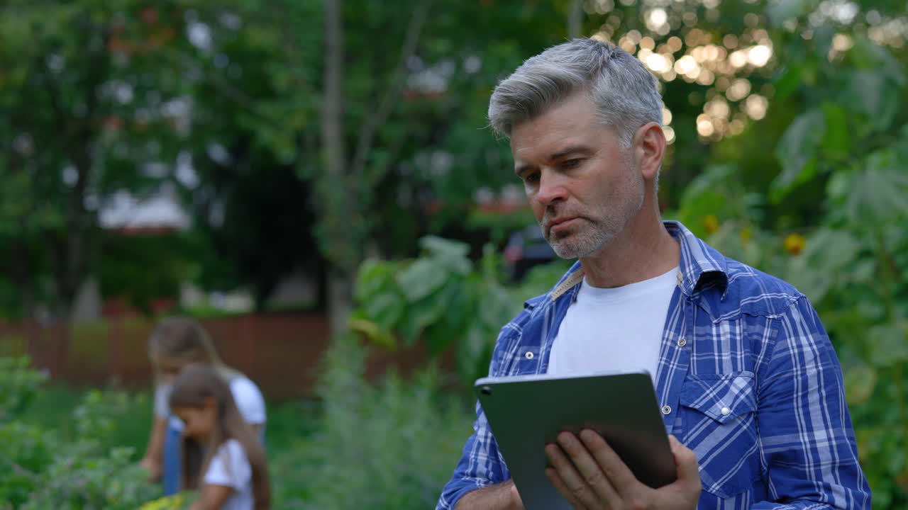 Father using tablet in the garden with children