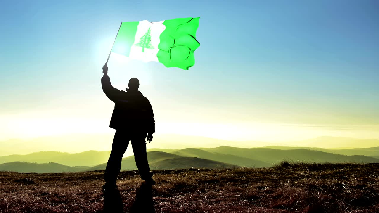 exitoso silueta hombre ganador agitando bandera de la isla de norfolk en la parte superior del pico de la montaña, fondo de bucle cinemagraph