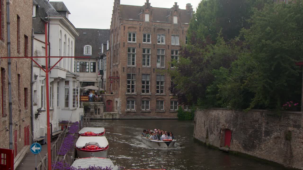 Tourists enjoy a boat tour on Bruges canal, passing old brick buildings under soft daylight