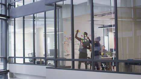 diverse male and female work colleagues brainstorming using glass wall in meeting room