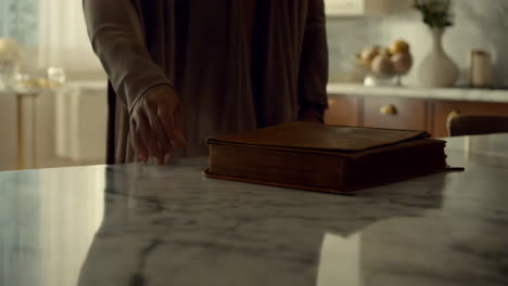 person's hand near an old book on a marble table