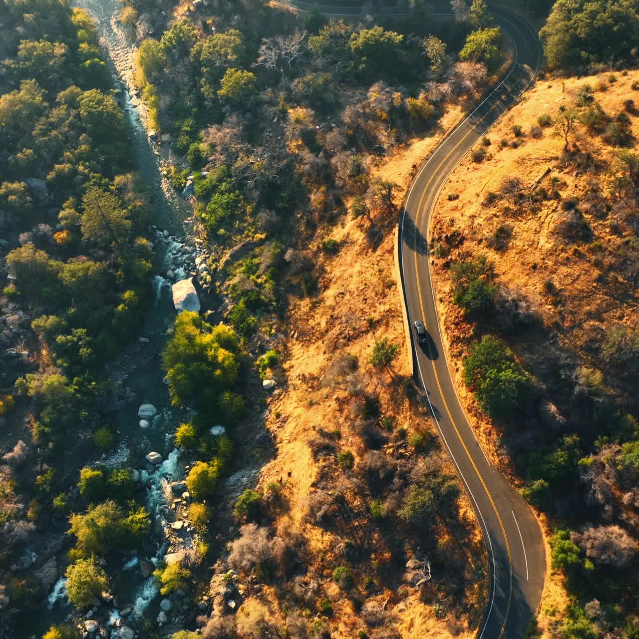 Car moving by the dangerous road on the mountain. Quick river with multiple rapids flowing at the foot. Top view