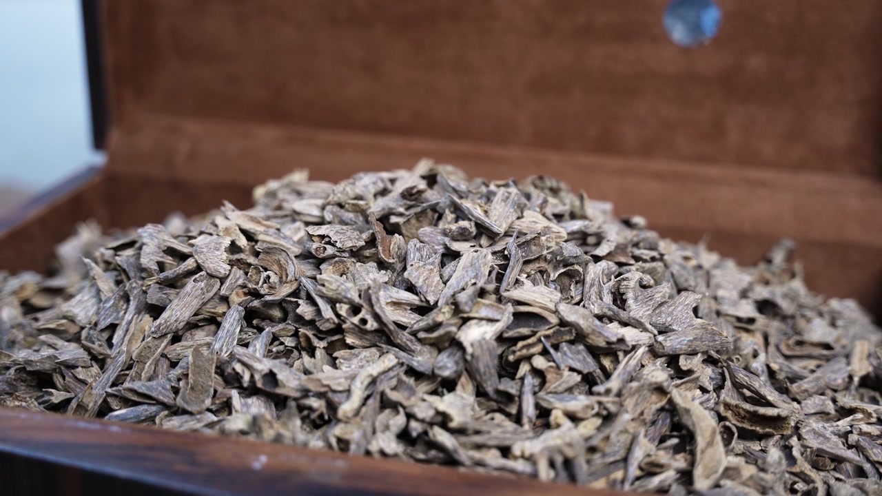 Close-up static shot of a large pile of aromatic Agarwood Oud chips stored in a lined wooden box. Perfect for luxury perfume ads and traditional Middle Eastern cultural content.