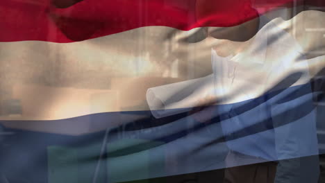 animation of flag of netherlands over biracial engineer with blueprints inspecting floor plan