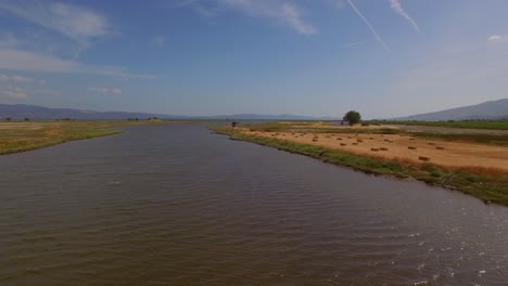 Aerial:-A-river-delta-with-a-road-bridge-passing-through-and-some-agricultural-buildings