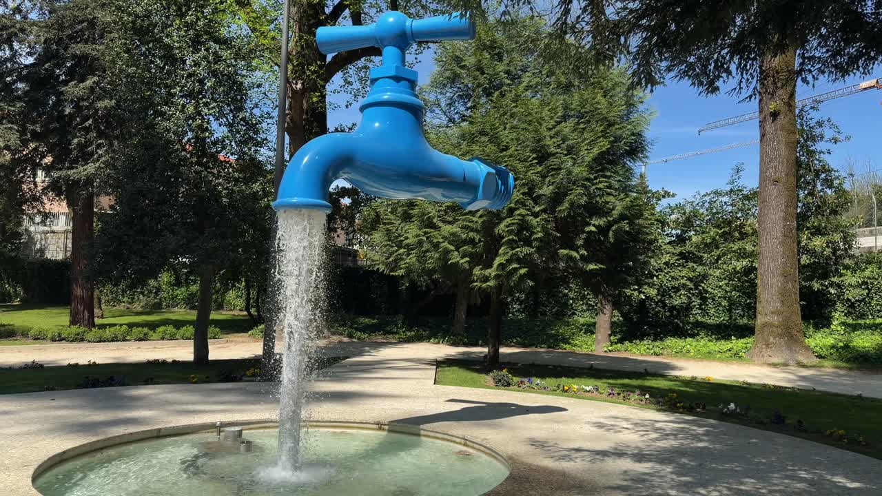 Grande rubinetto blu che versa acqua in una fontana circondata da alberi in un parco