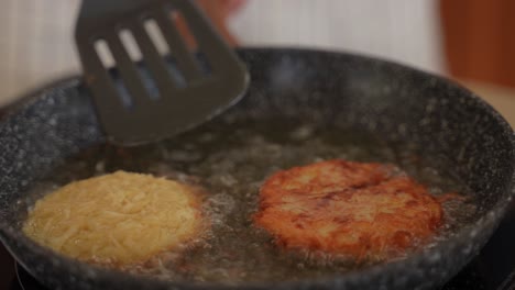 close-up of frying fresh homemade hashbrown potato puffs in oil as they are being flipped with a spatula