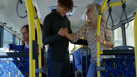 pasajero masculino ayudando a un pasajero maduro a levantarse mientras viaja en el autobús 4k