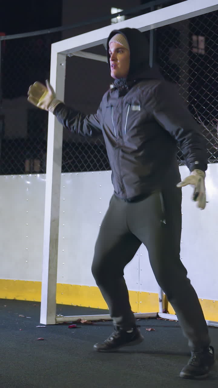 portero con ropa deportiva y guantes entrenando cerca del poste de la portería durante la sesión nocturna centrándose en las habilidades de captura y agilidad con un entorno urbano iluminado