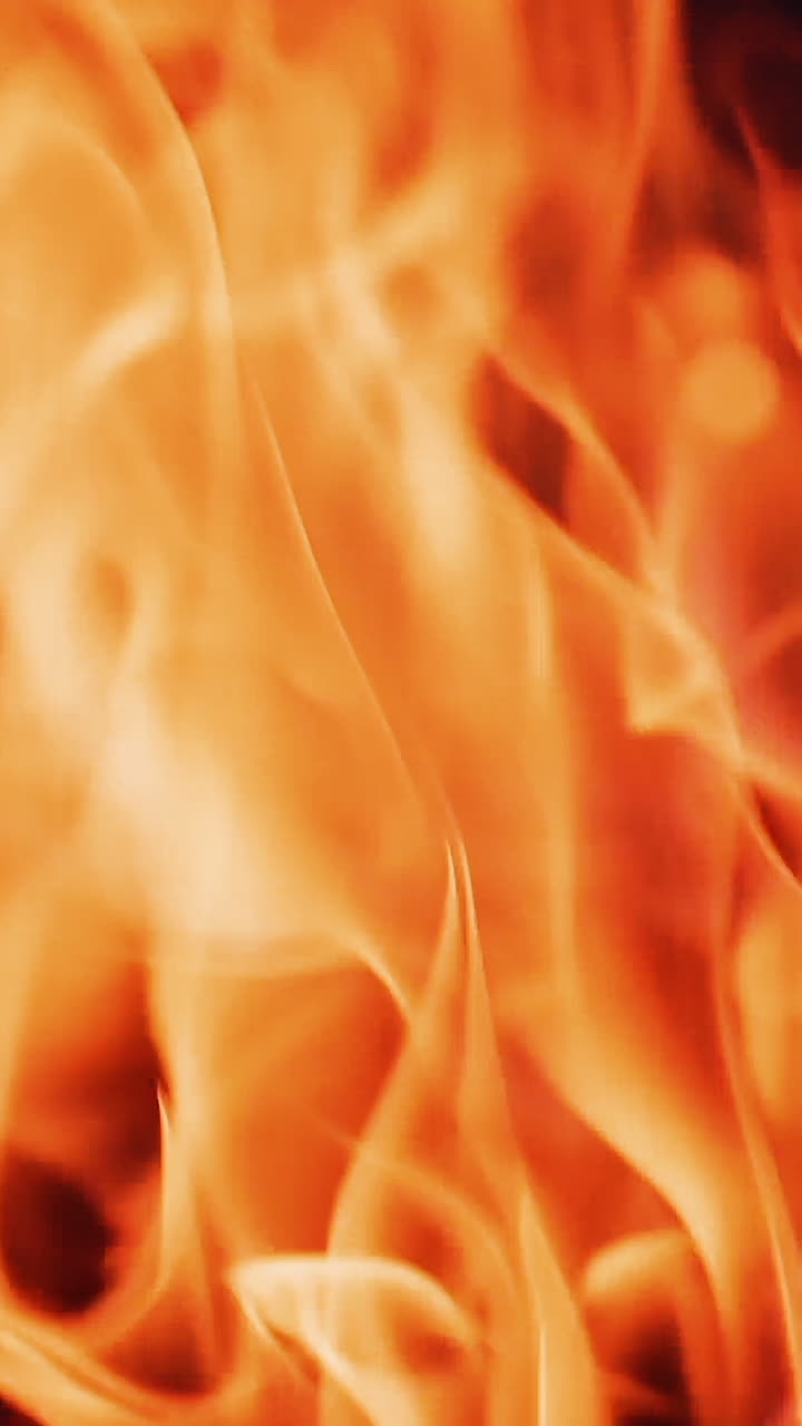 Beautiful fire background. Red and yellow flame of bonfire at dusk. Bright flame of vivid tongues dancing in slow motion. Close-up. Vertical video