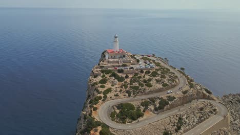 an aerial view of a lighthouse perched on a high rocky cliff, connected by a winding coastal road. the vast expanse of calm blue sea stretches endlessly into the horizon.
