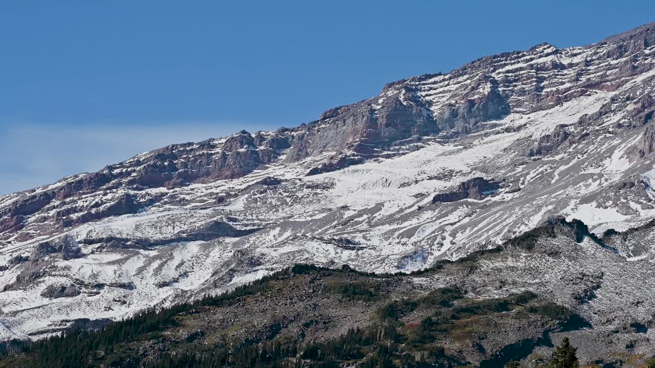Aerial view of rugged snow-lined mountain slope transitioning into alpine forest below