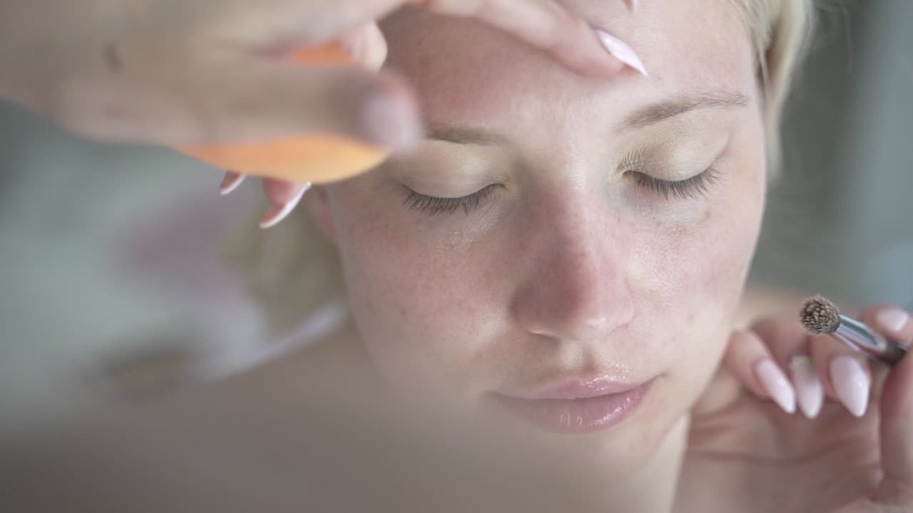 Blond women getting slowly careful eye shadow primer dispersed with sponge on natural face without make up - close up shot from above cinematic