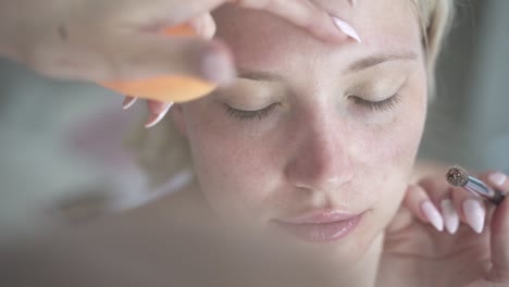 blond women getting slowly careful eye shadow primer dispersed with sponge on natural face without make up - close up shot from above cinematic