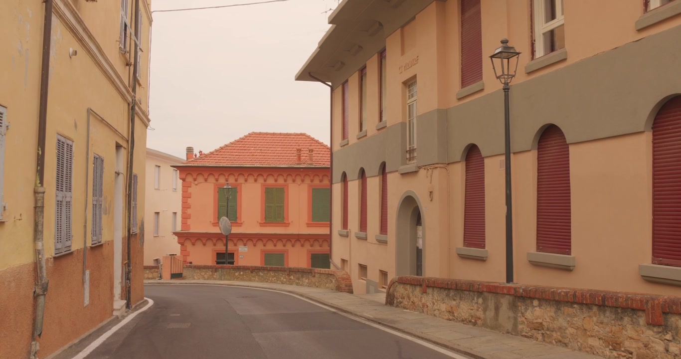 Una calle tranquila y curva discurre entre edificios residenciales de colores pastel con persianas y una farola en el casco antiguo de Imperia, Porto Maurizio, Riviera Italiana, Italia