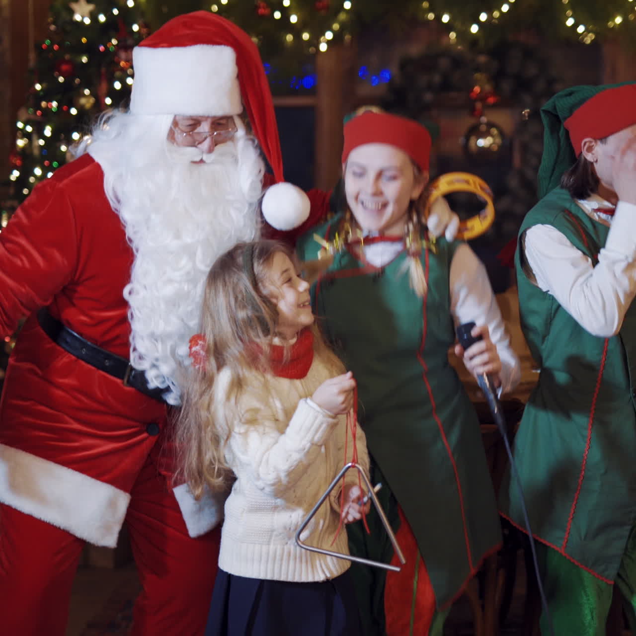 Festive atmosphere in Santa's residence. Santa Claus, two elves and children dancing and singing together at Christmas.