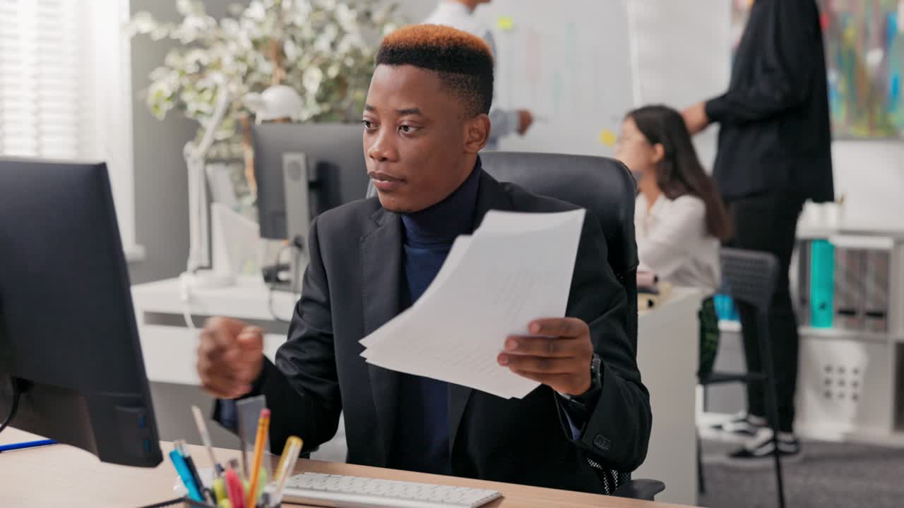 Office worker sits in front of computer at desk has video call, internet connection through webcam, shows paper document with billing that guy explains to co-worker